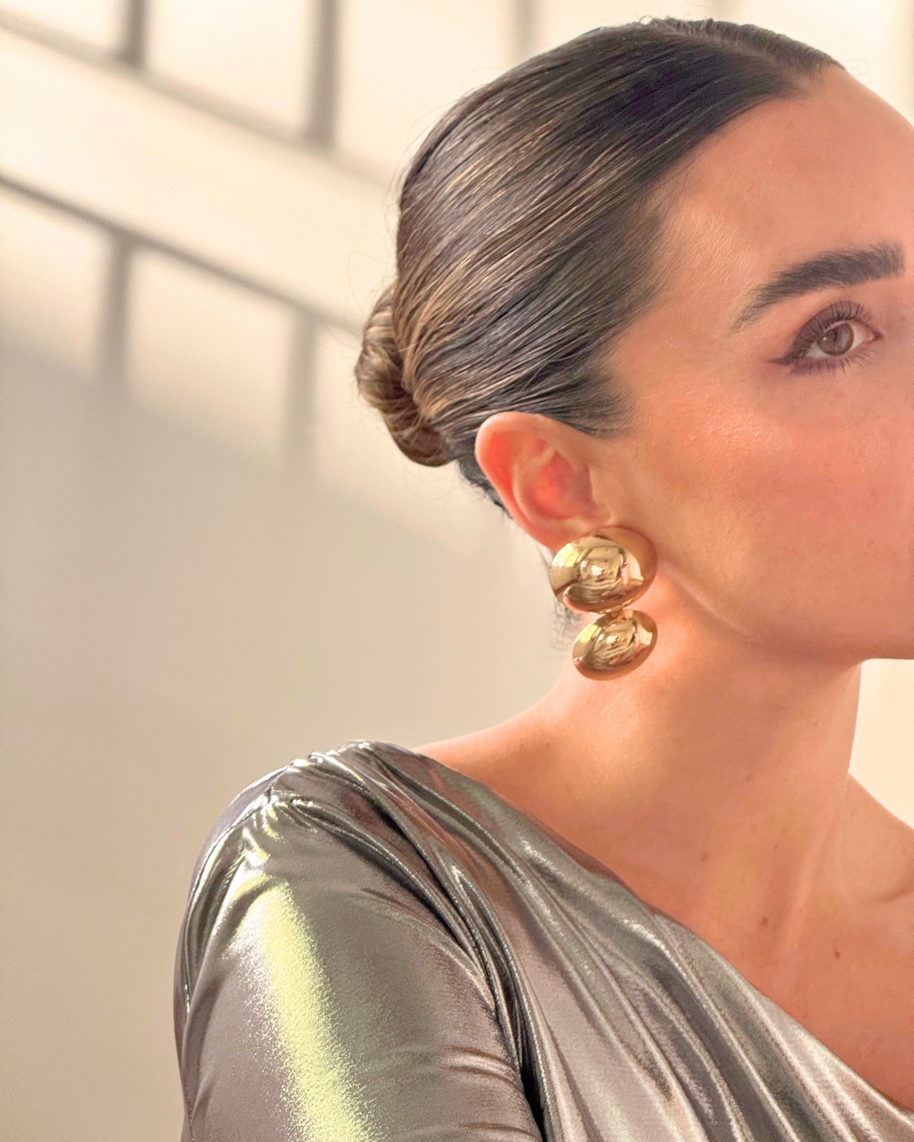 A pair of gold earrings from AUKA STUDIO's BAZEL collection, featuring sleek and elegant jewelry design with shiny gold finish.