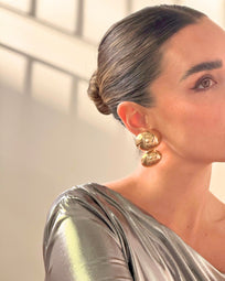 A pair of gold earrings from AUKA STUDIO's BAZEL collection, featuring sleek and elegant jewelry design with shiny gold finish.