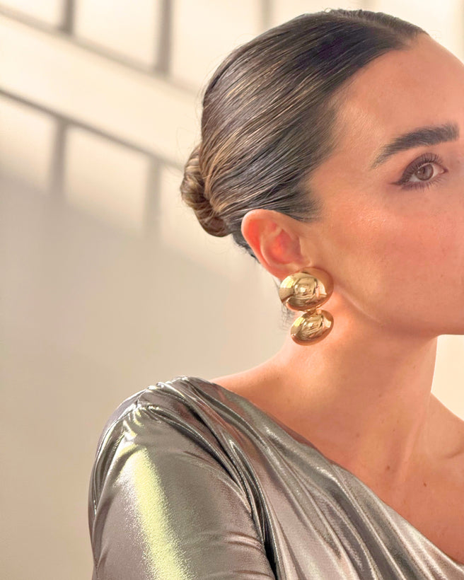 A pair of gold earrings from AUKA STUDIO's BAZEL collection, featuring sleek and elegant jewelry design with shiny gold finish.