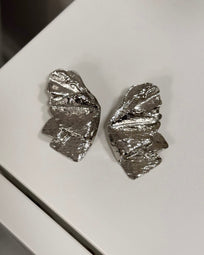A pair of AUKA STUDIO BERA silver earrings with sleek, minimalist design, displayed against a neutral background.